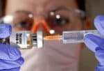 In this illustration, a medical technicia holds a small bottle labelled with a "Vaccine COVID-19" sticker and a medical syringe. Photo: CNS Illustration/ Reuters