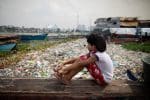 A girl sits on a piece of wood as she looks out over a trash-filled Manila Bay in 2020. Photo: CNS/Eloisa Lopez, Reuters