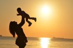 silhouette photo of a mother carrying her baby at beach during golden hour