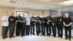 Group of clergy in black clerical clothes standing in a hallway, giving thumbs up.