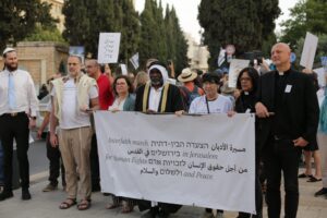 Group of diverse faith demonstrators marching in Jerusalem, holding a large banner calling for human rights and peace.