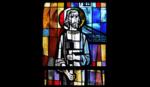 Stained-glass window depicting a haloed bearded figure in white robes with folded hands.