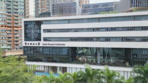 Saint Francis University building with a glass-fronted facade, surrounded by tall apartment blocks and palm trees in the foregroundand background cityscape