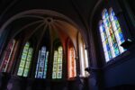 Interior of a church with tall colorful stained-glass windows along vaulted arches, light filtering through the nave.