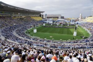 Crowded stadium during a formal event with a central stage on the grass field.