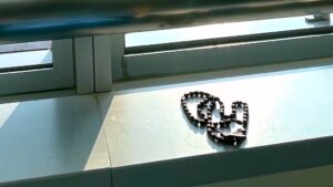 Beaded rosary laid on a metal windowsill, forming a heart shape by the window.