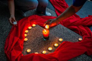 Memorial vigil setup with a circle of tea-light candles around a central red candle on red fabric.