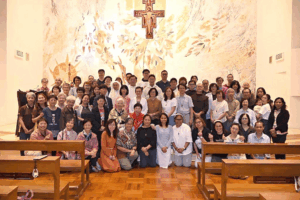 Large group of people posing for a photo inside a church with a mural and cross behind them.] The first option seems to include a stray bracket; I'll provide clean version below.