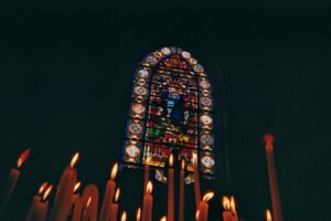 Stained-glass window illuminated by flickering candles in a dark church interior.