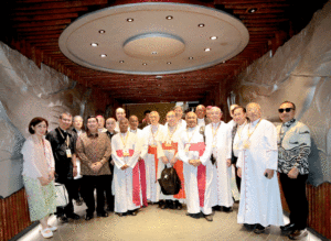 Group of priests and clergy in white robes posing for a photo in a hallway.