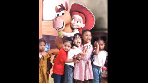 Group of smiling children posing with two large cartoon mascots indoors.