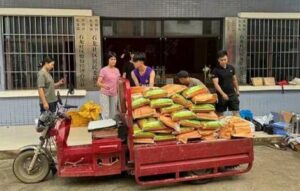 People stand around a red cart loaded with stacked sacks of grain outside a building with barred windows and signage in Chinese.