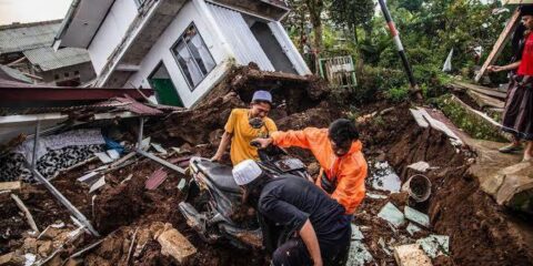 Rescuers move a motorcycle through mud and debris amid a collapsed home after a disaster.
